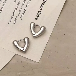 Detailed view of polished silver heart-shaped hoop earrings on a textured minimalist background