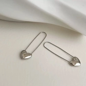 Silver heart pendant earrings with long U-shaped hooks on a white satin background
