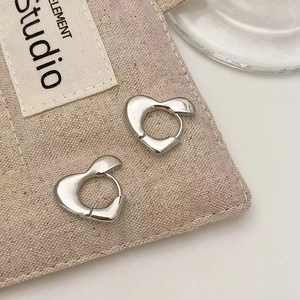 Close-up of heart-shaped silver earrings on canvas texture, showing shiny metallic finish