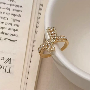 Detail of elegant gold bow ring with pearls and rhinestones on white porcelain