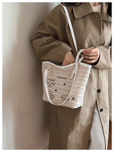 Détail d'un sac cabas tissé beige avec broderie de chat et anses en cuir blanc