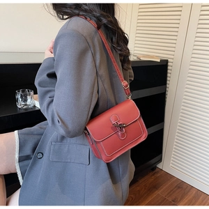 Detail of red leather crossbody bag featuring white stitching and vintage metal buckle