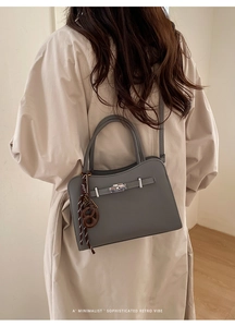 Detail of dark grey textured crossbody bag with a brown pretzel pendant on model
