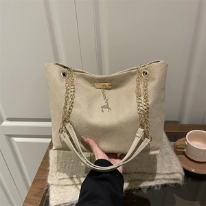 Beige woven tote bag with gold chain strap and deer pendant in a cozy cafe setting