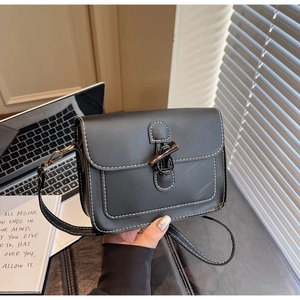 Detail of a black crossbody bag with white contrast stitching and horn buckle closure
