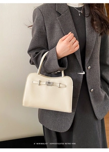 Detail of beige textured leather handbag with silver twist lock on dark grey blazer