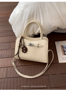 Detail of off-white lychee grain leather handbag with gold twist lock and brown bow charm