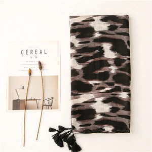 Detalle de bufanda suave con estampado de leopardo y borlas negras en fondo minimalista