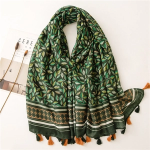 Détail d'une écharpe vert foncé avec motifs de feuilles, bordures et pompons colorés