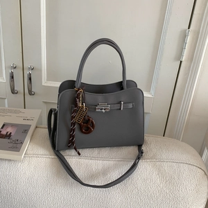 Gray lychee grain leather tote bag with pretzel charm on a chic tweed sofa background