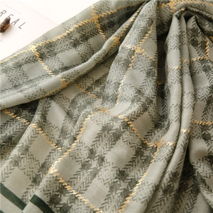 Detailed close-up of grey-green linen scarf with gold metallic grid and fringe textures