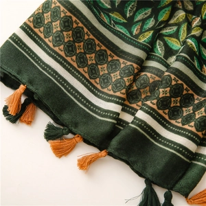 Détail d'une écharpe vert forêt avec motif de feuilles, bords jacquard et glands faits main