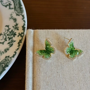 Detailed macro view of gold butterfly stud earrings with green crystals and small white gems