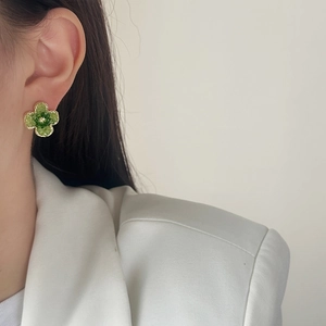 Elegant gold-edged green four-leaf clover stud earrings worn by a female model