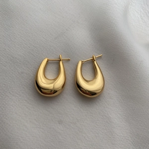 Boucles d'oreilles dorées en forme de U avec finition polie sur tissu blanc