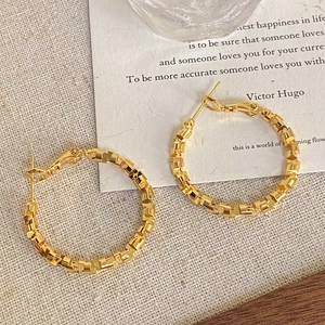 Detailed view of gold geometric hoop earrings with textured cubic pattern on beige linen