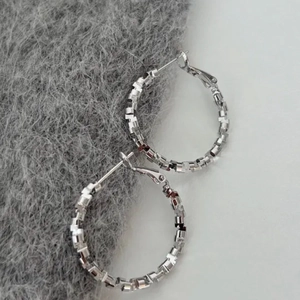 Silver hoop earrings with geometric textured metal segments on grey plush background