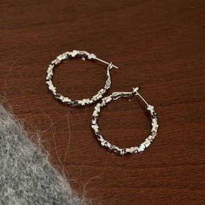 Macro detail of silver geometric textured hoop earrings on a vintage wooden surface