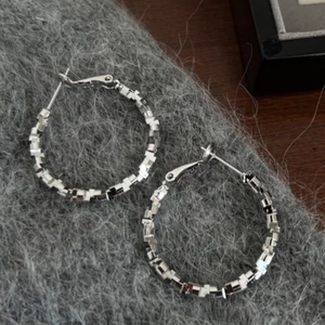 Macro shot of silver hoop earrings featuring a geometric textured mosaic design