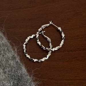 Macro shot of silver hoop earrings featuring modern 3D geometric block textures