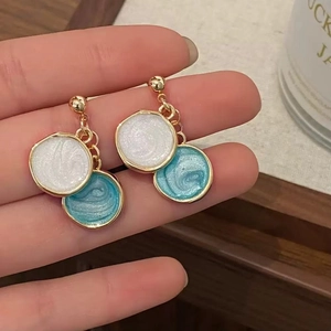 Détail de boucles d'oreilles en émail bleu et blanc avec base dorée tenues à la main