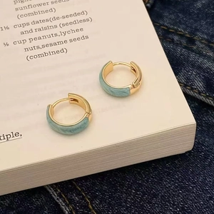 Gros plan de boucles d'oreilles créoles dorées en émail bleu clair sur un livre ouvert