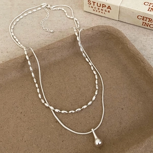 Close-up of double-layer silver teardrop pendant necklace on rustic ceramic tray
