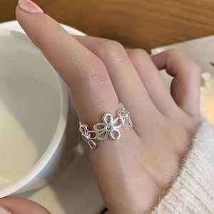 Dettaglio anello a fiore traforato in argento con zirconi indossato su uno sfondo caldo