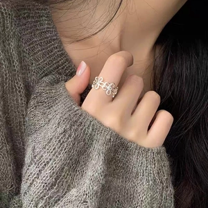 Dettaglio di un anello a fiori in argento traforato indossato su sfondo in maglia