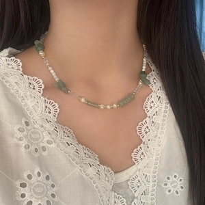 Detail of freshwater pearl and green gemstone necklace worn with white lace clothing