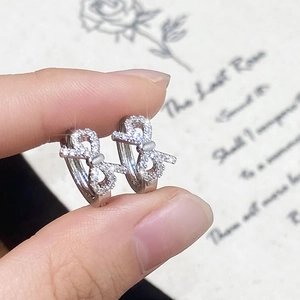 Détails de petites boucles d'oreilles nœud argentées serties de zircons brillants