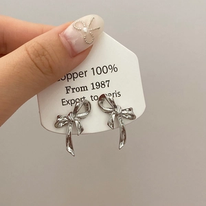 Détail de boucles d'oreilles nœud argentées au style métal liquide sur carte