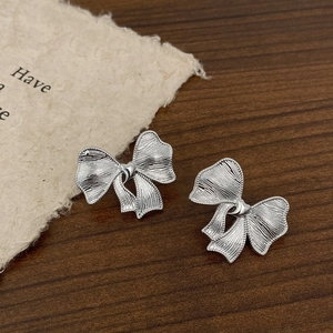 Détail de boucles d'oreilles nœud argenté avec texture et bordure perlée sur bois