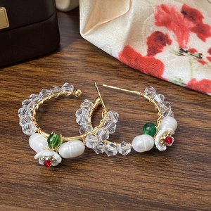 Detail of gold metal wire earrings with pearls, crystals and floral charms on wood