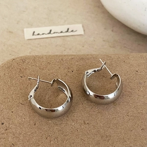 Close-up of polished silver geometric hoop earrings on a textured brown background