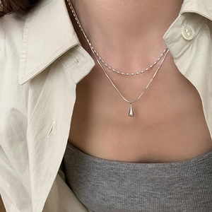 Close-up of minimalist double-layered silver necklace with a polished water drop pendant