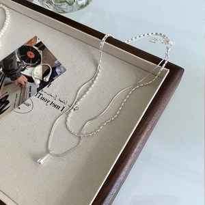 Detail of S925 sterling silver double-layer necklace featuring a droplet pendant on wood tray