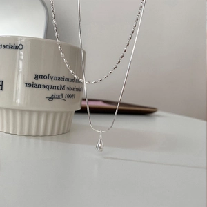 Close-up of double-layer silver necklace featuring a polished water drop pendant