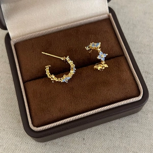 Macro shot of gold C-shaped earrings with blue floral stones in a velvet box