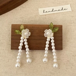 Détail de boucles d'oreilles fleurs avec pétales en résine et pompons en perles sur bois