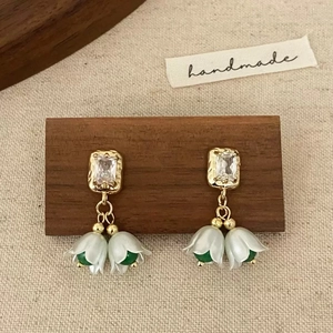 Détail de boucles d'oreilles dorées avec fleurs de muguet blanches et zircon cubique