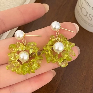 Détail de boucles d'oreilles fleurs avec pierres vertes et perles blanches sur fil doré