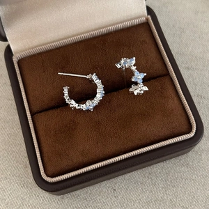 Macro view of C-shaped silver earrings with blue zircon stones on dark velvet