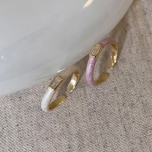 Detail of cream enamel adjustable rings with rectangular zirconia on linen background