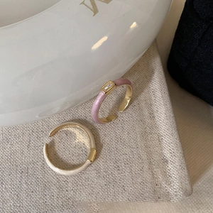 Detail of light purple and cream enamel open rings with gold plating on textured fabric