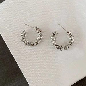Detail of silver hoop earrings featuring unique layered irregular metallic textures