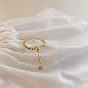 Macro detail of gold star charm ring with zircon stones on soft cream fabric