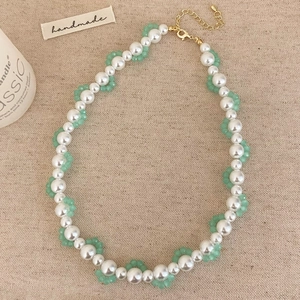 Detail of handmade pearl necklace with green beads and gold lobster clasp on linen