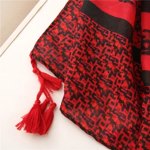 Détail d'une écharpe géométrique rouge et noire avec des finitions à glands élégants