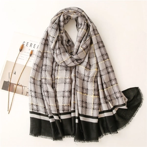 Gray and black plaid scarf with yellow stripes and fringe on a minimalist white backdrop